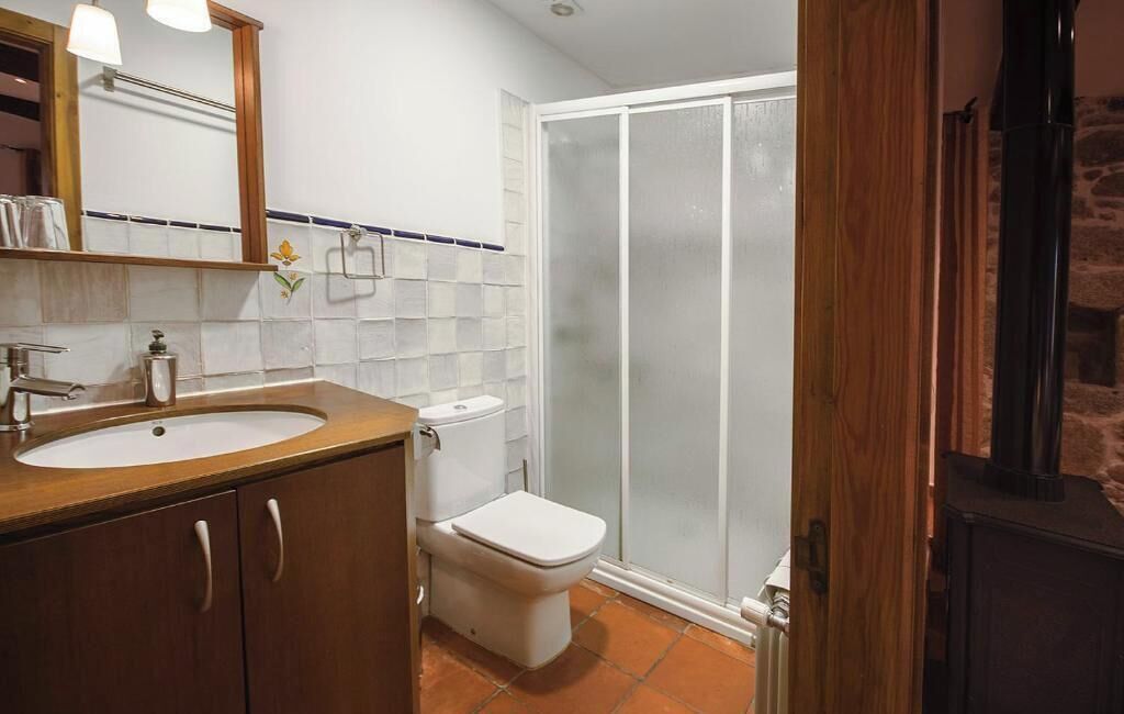 A bathroom with a wooden vanity, a white sink, a toilet, and a glass shower enclosure.