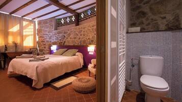 A bedroom with a stone wall, a bed with a headboard, a bedside table, and a bathroom with a toilet.