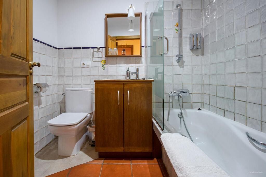 A bathroom with a toilet, a wooden cabinet, a glass shower enclosure, and a bathtub.