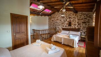 A bedroom with two beds, wooden flooring, stone walls, a wooden ceiling, and skylights.
