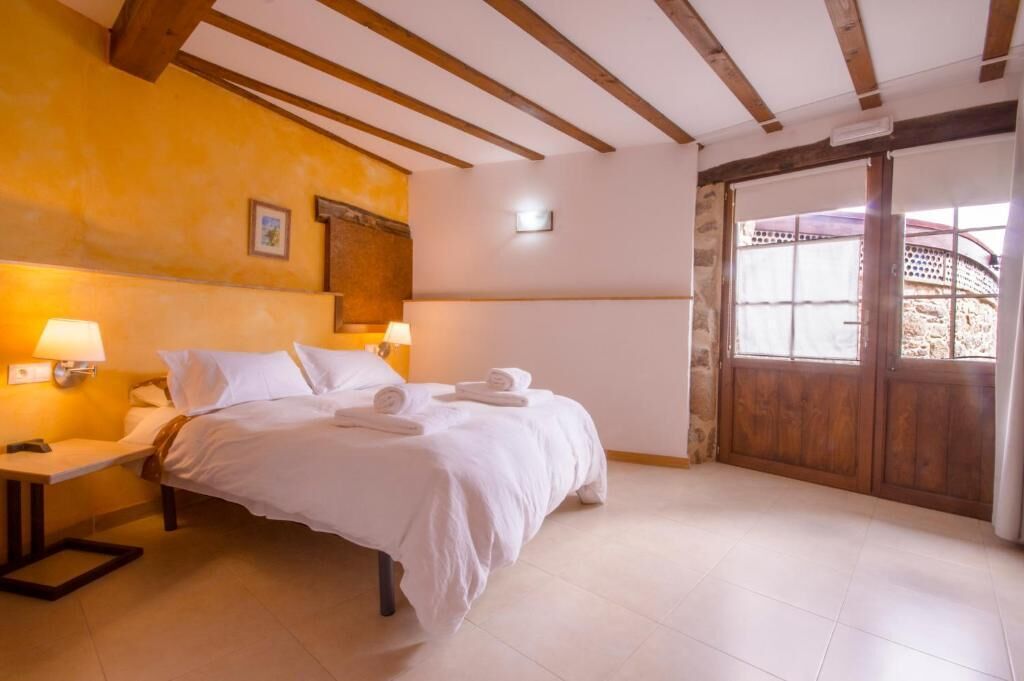 A hotel room with a bed, bedside lamps, a wooden door, and a view through the door.