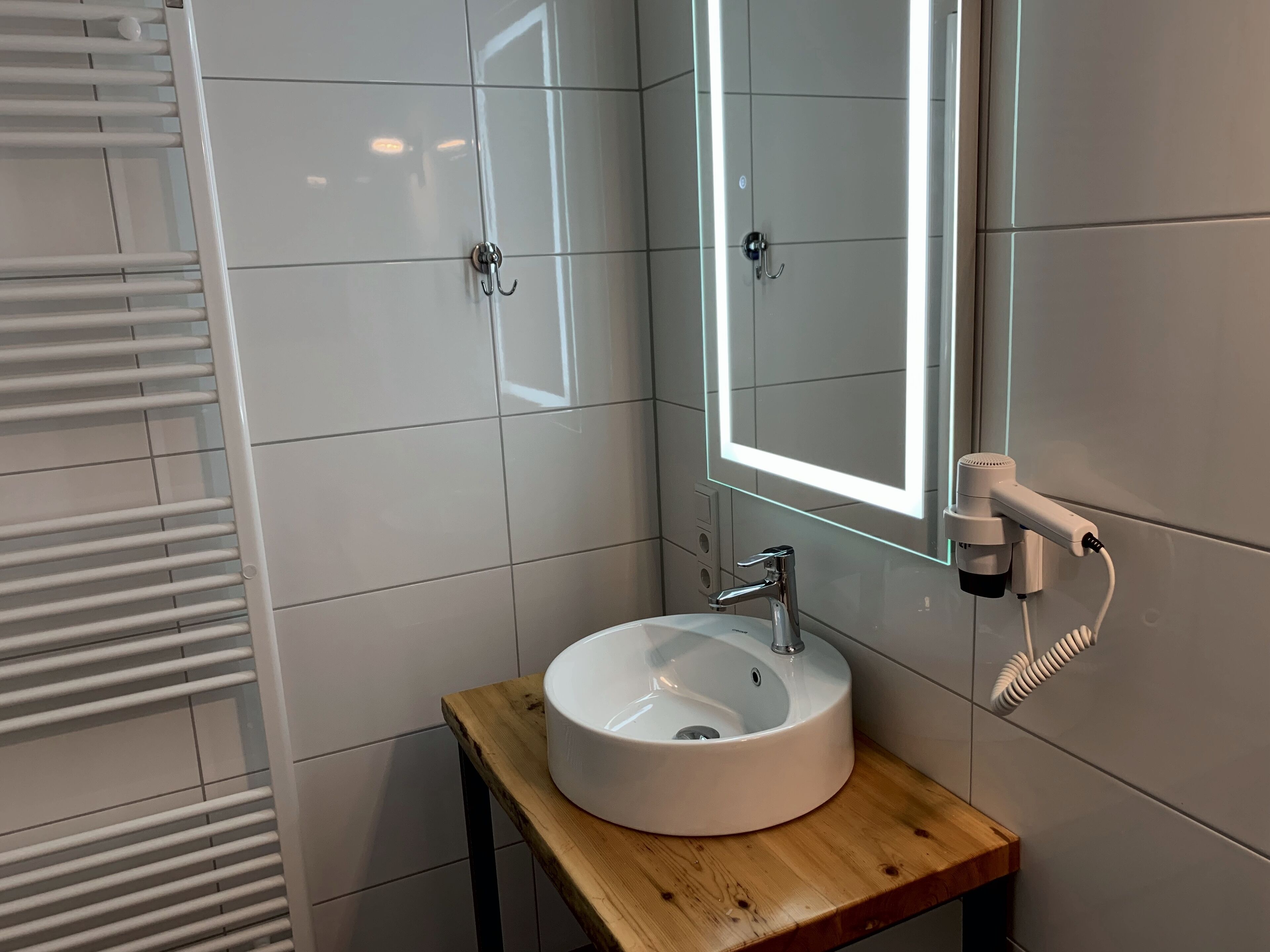 A bathroom with a white sink, a mirror with a light, and a towel rack.