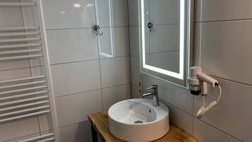 A bathroom with a white sink, a mirror with a light, and a towel rack.