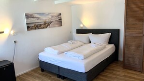 A neatly made bed with white linens and towels, a dark headboard, and a painting of a beach scene on the wall. - TaT Hotel (Rheine)