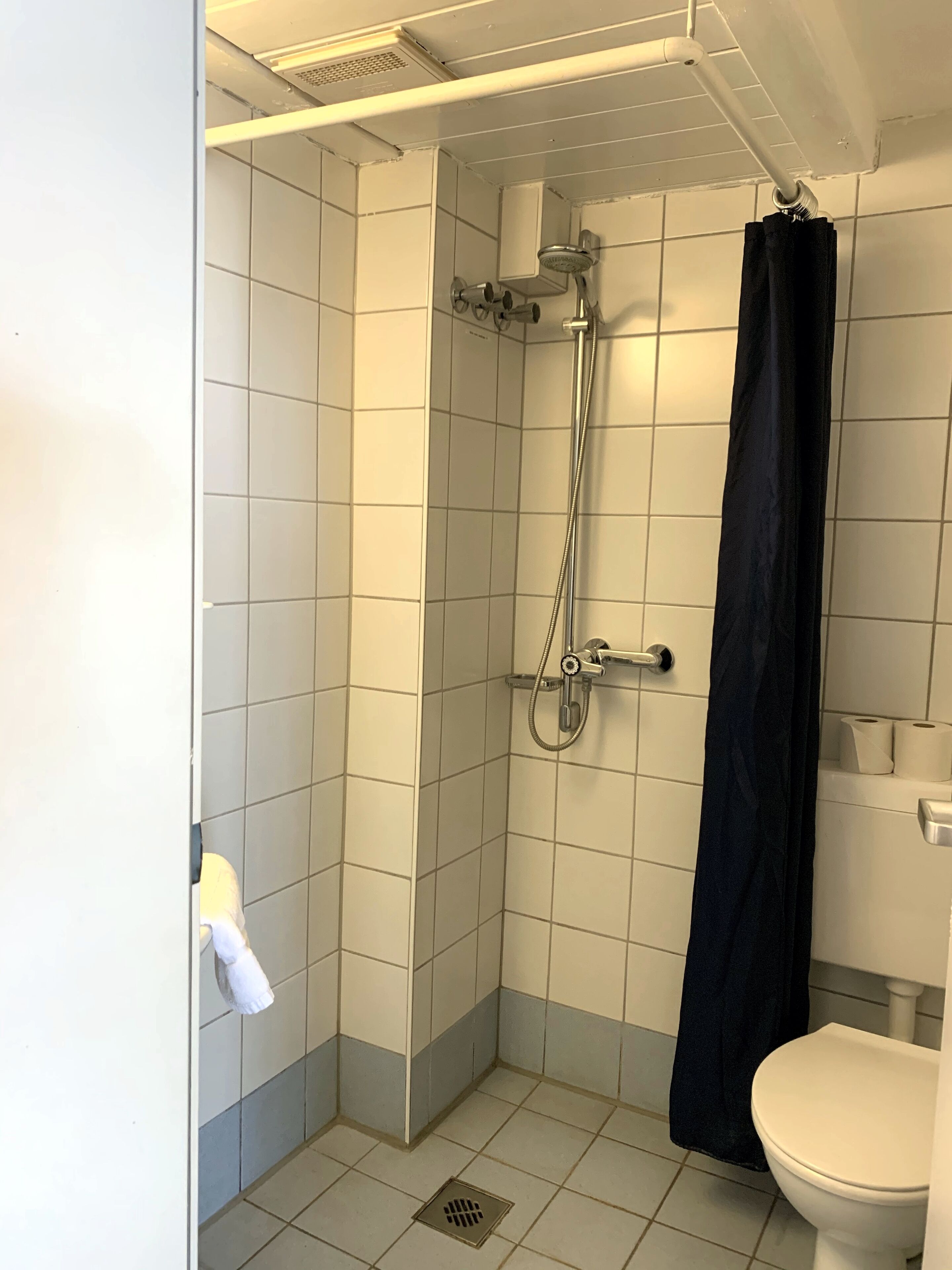 A small, tiled bathroom with a shower, toilet, and towel rack.