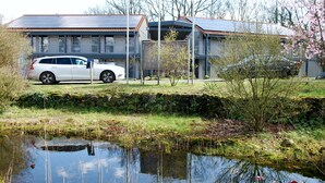 A residential building with a car parked in front, a small pond, and a garden area with trees and shrubs. - TaT Hotel (Rheine)