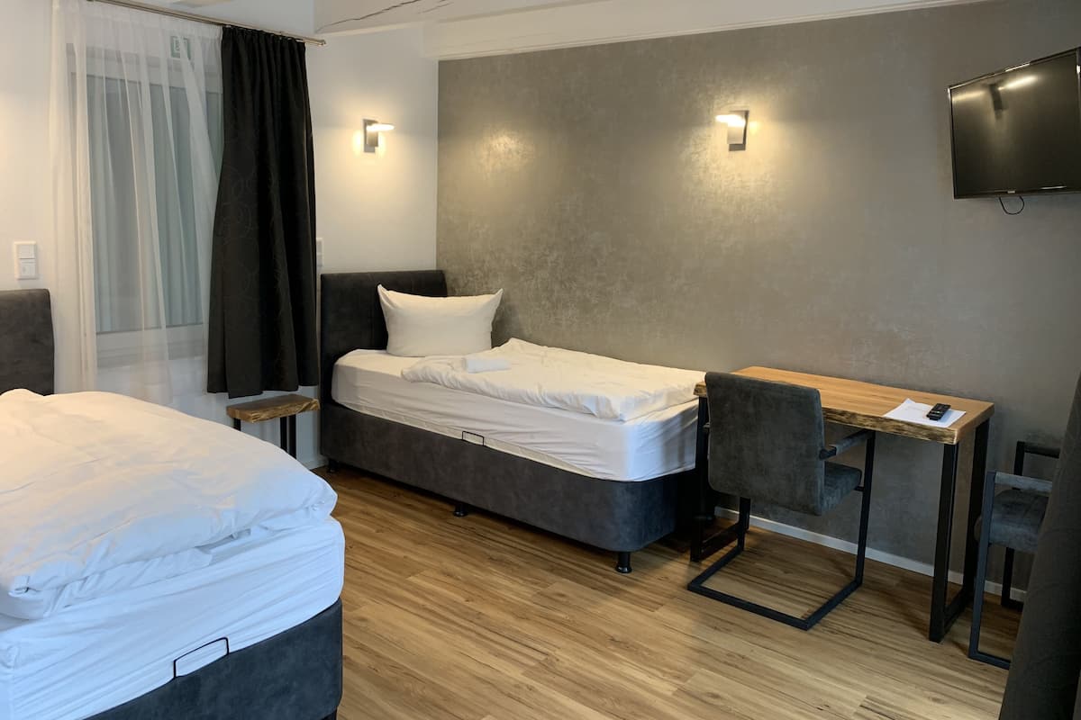 Ein Hotelzimmer mit Bett, Schreibtisch, Stuhl und einem an der Wand befestigten Fernseher.