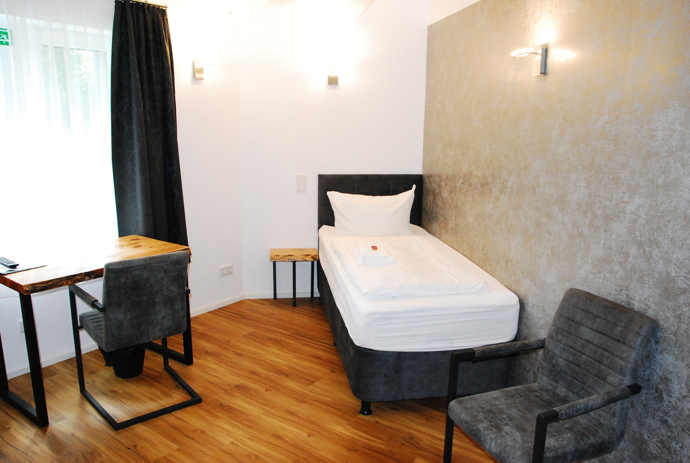 Une petite chambre moderne, équipée d’un lit simple, d’un bureau et de deux chaises.
