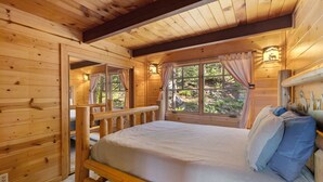 Une chambre rustique en bois, avec un lit, une fenêtre avec des rideaux et une vue sur l’extérieur.