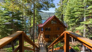 Une cabane en bois avec un toit rouge, entourée de grands arbres et bordée par un lac.