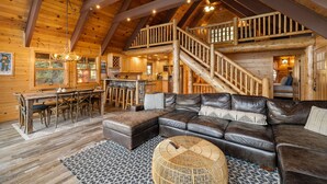 L’intérieur d’une cabane en rondins, avec un escalier en bois, un grand canapé en cuir et un coin repas.