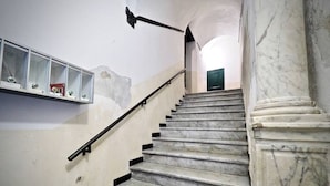 Uma escadaria de mármore com corrimão, uma vitrine de vidro com objetos e uma porta verde no topo.
