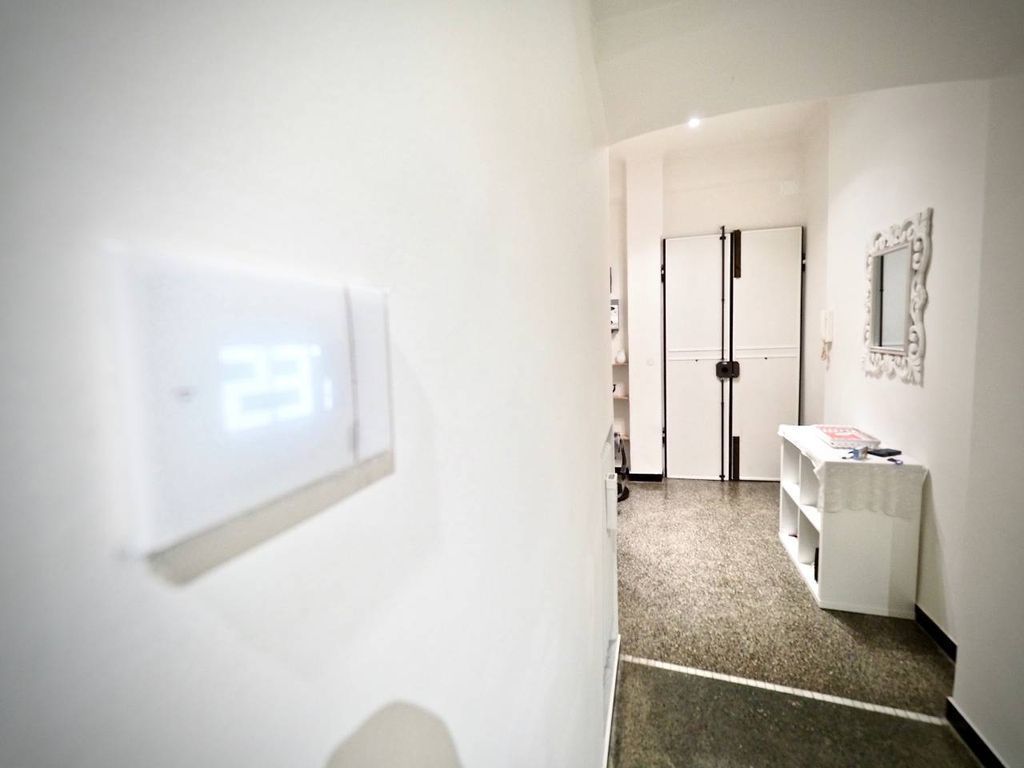 A hallway with a white wall, a light switch, a door, and a small table with a mirror.
