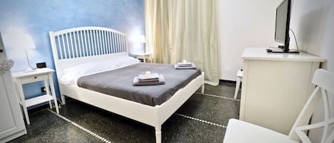 A bedroom with a bed, a desk, a chair, a TV, and a window with curtains.