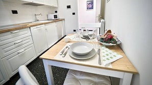 Cozinha pequena e limpa, com armários brancos, bancada de madeira e um espaço de refeições com mesa posta para dois.