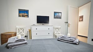 Quarto com cama, televisão, cômoda e duas quadros pendurados na parede.
