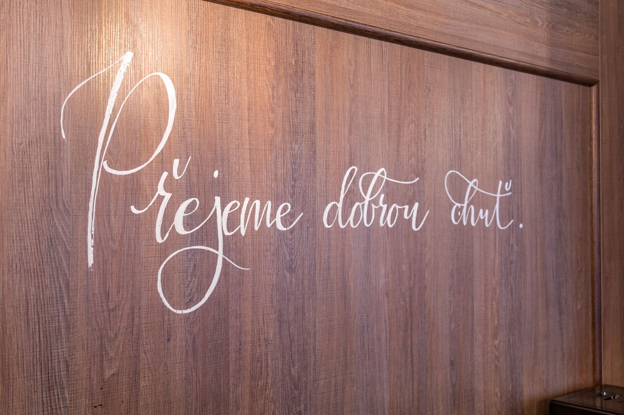 A wooden wall with a white cursive sign that reads "Prejeme dobrou chut."