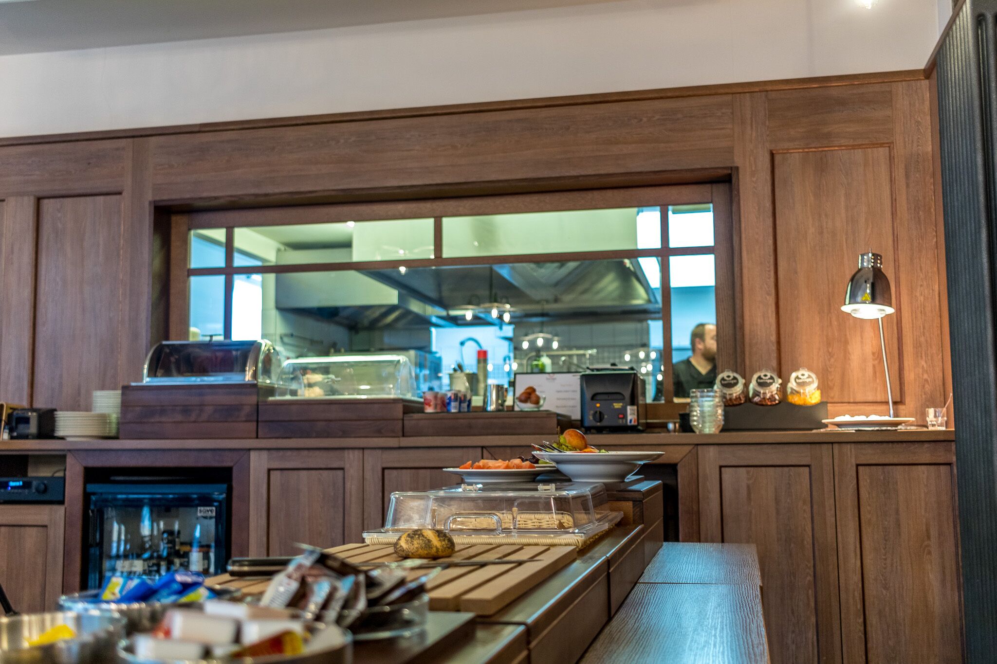 A kitchen area with wooden cabinets, a large window, and various food items on the counter.