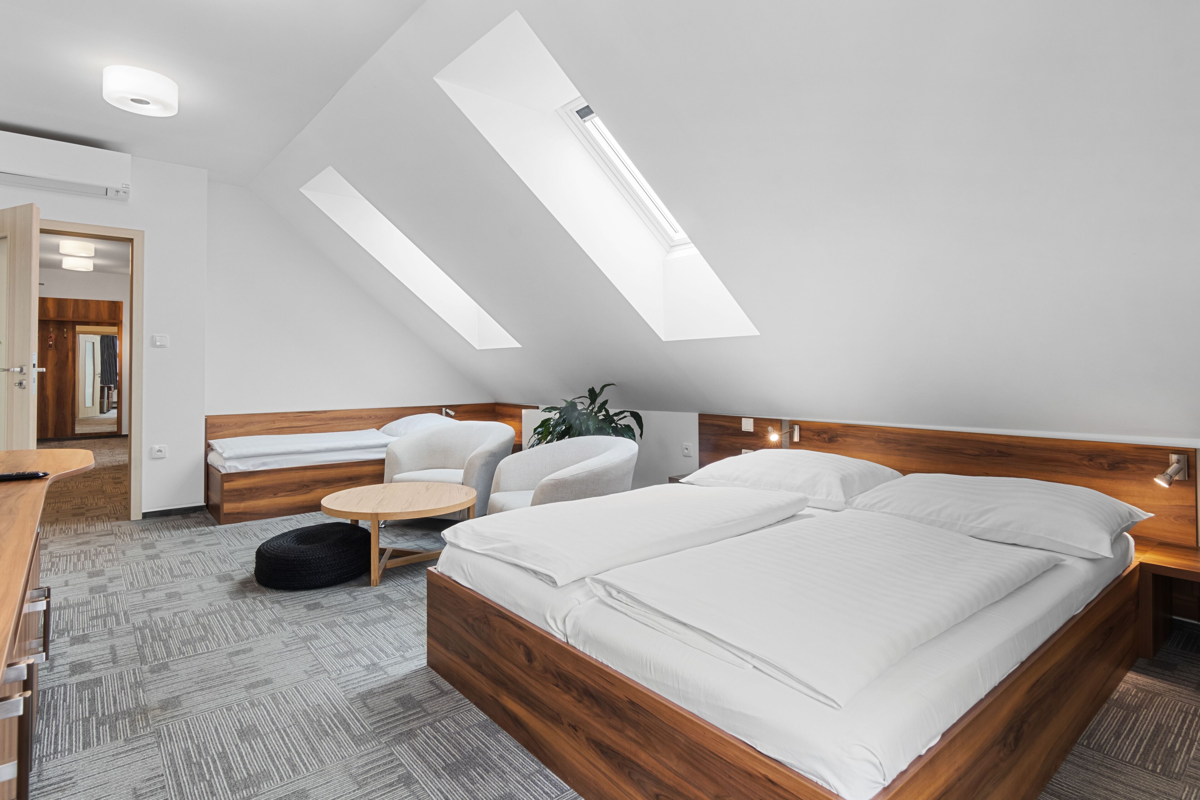 A modern bedroom with a skylight, a bed, a desk, and a chair.