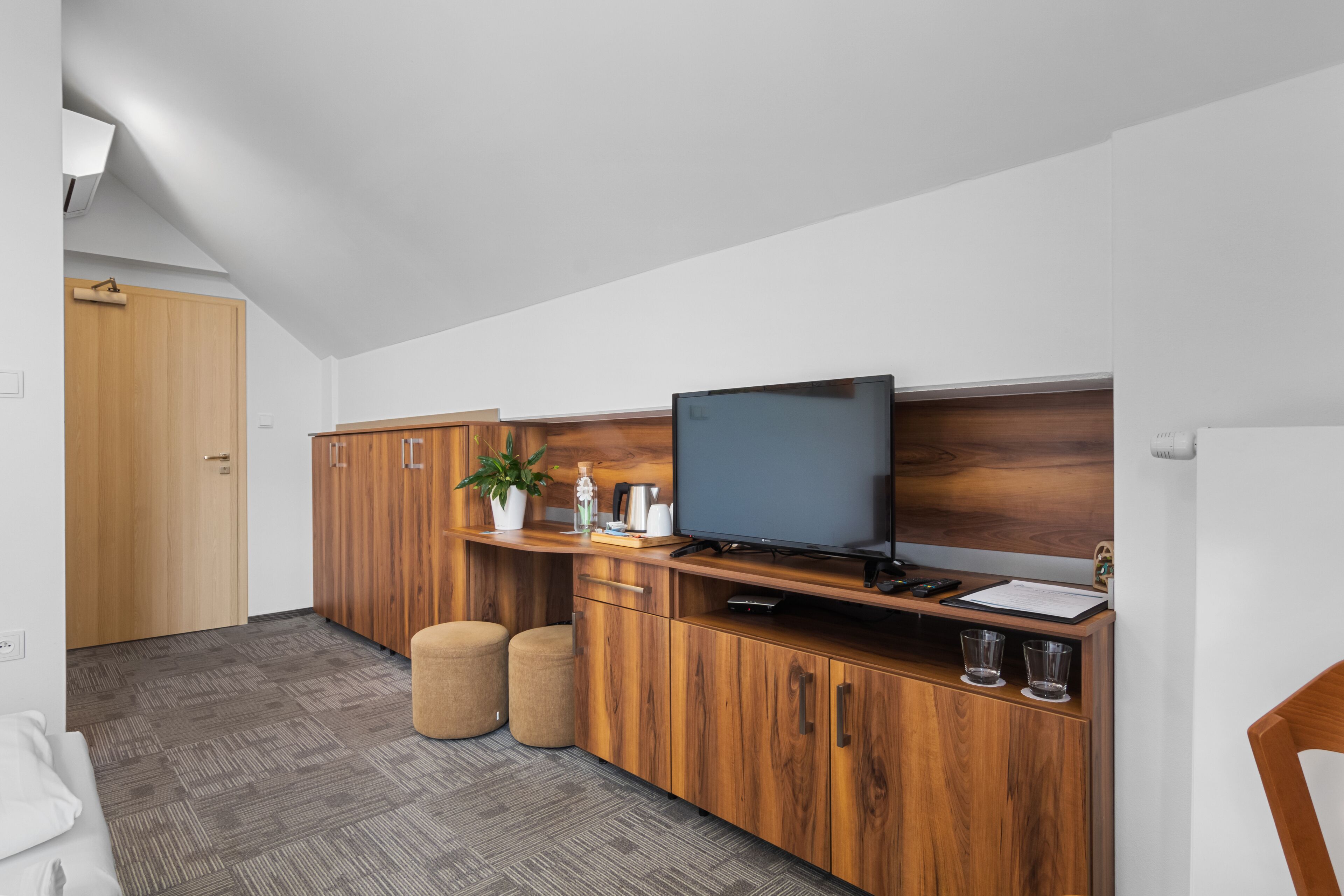 A modern kitchen with wooden cabinets, a built-in TV, and a small seating area with ottomans.