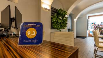 Una recepción con una placa azul de reconocimiento de Booking.com, una planta en maceta y vista al vestíbulo.