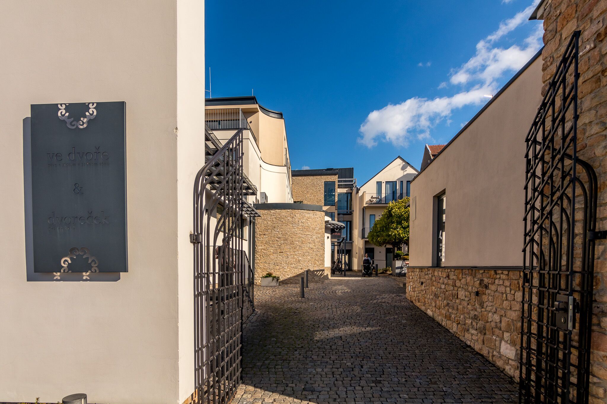 A cobblestone street with buildings on either side, a metal gate, and a clear blue sky.