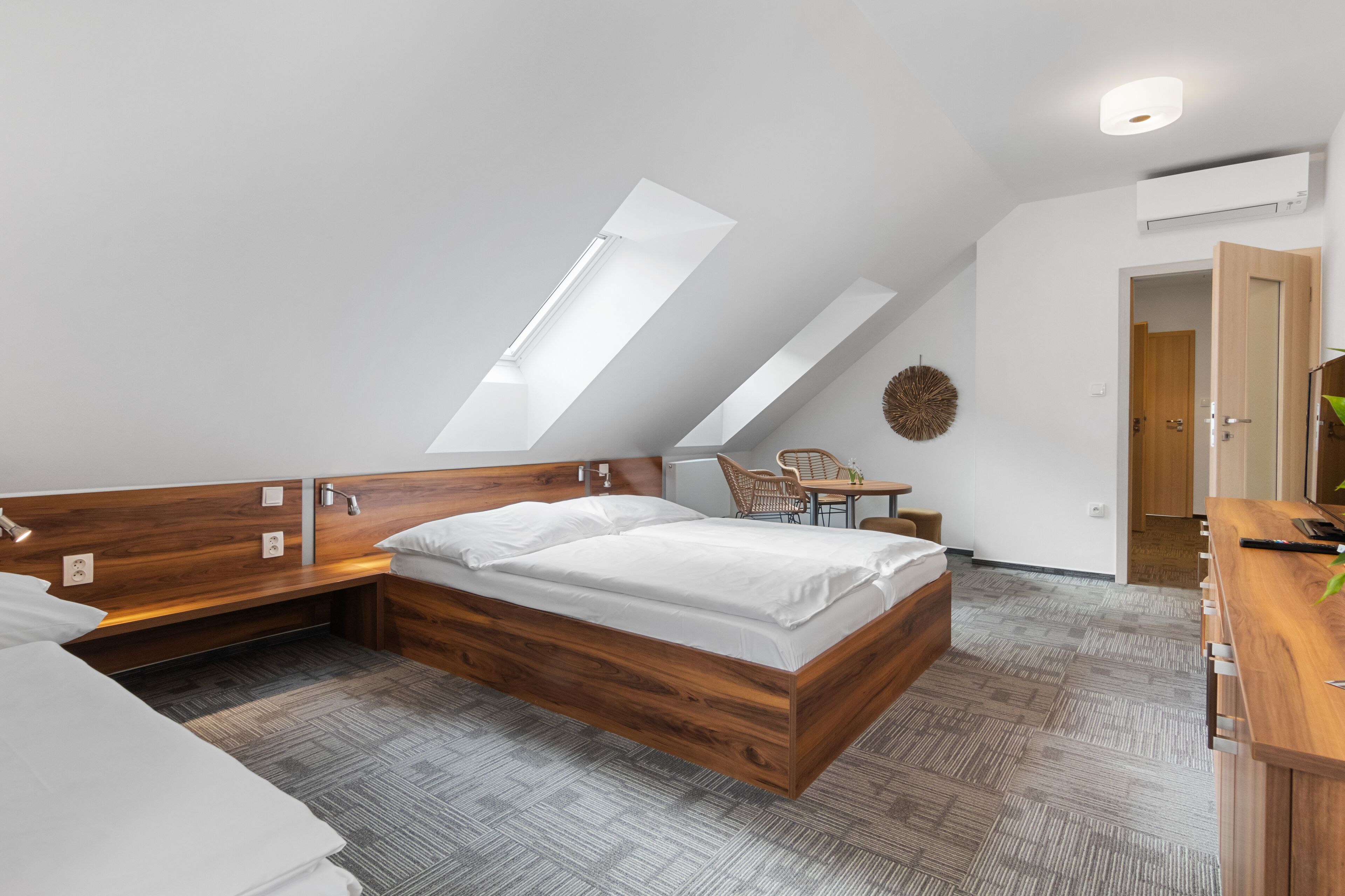 A modern bedroom with a sloped ceiling, a wooden bed frame, a small desk, and a chair.