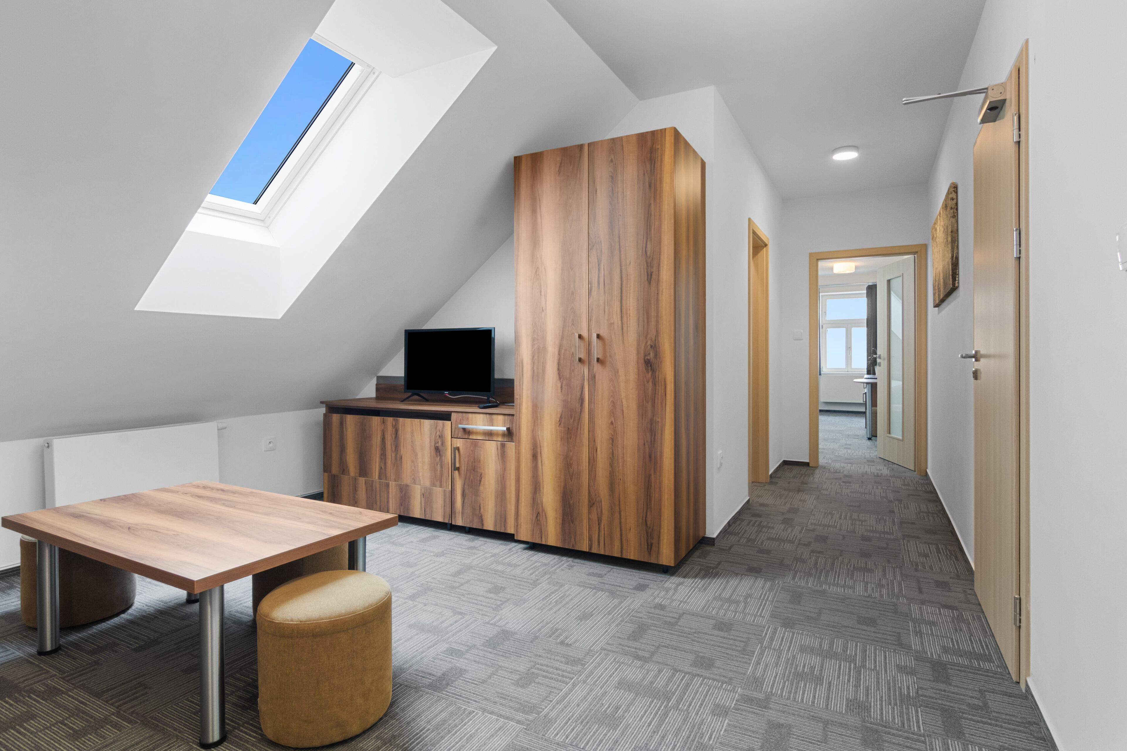 Una habitación moderna con techo inclinado, un armario de madera, una mesita pequeña y un banco.