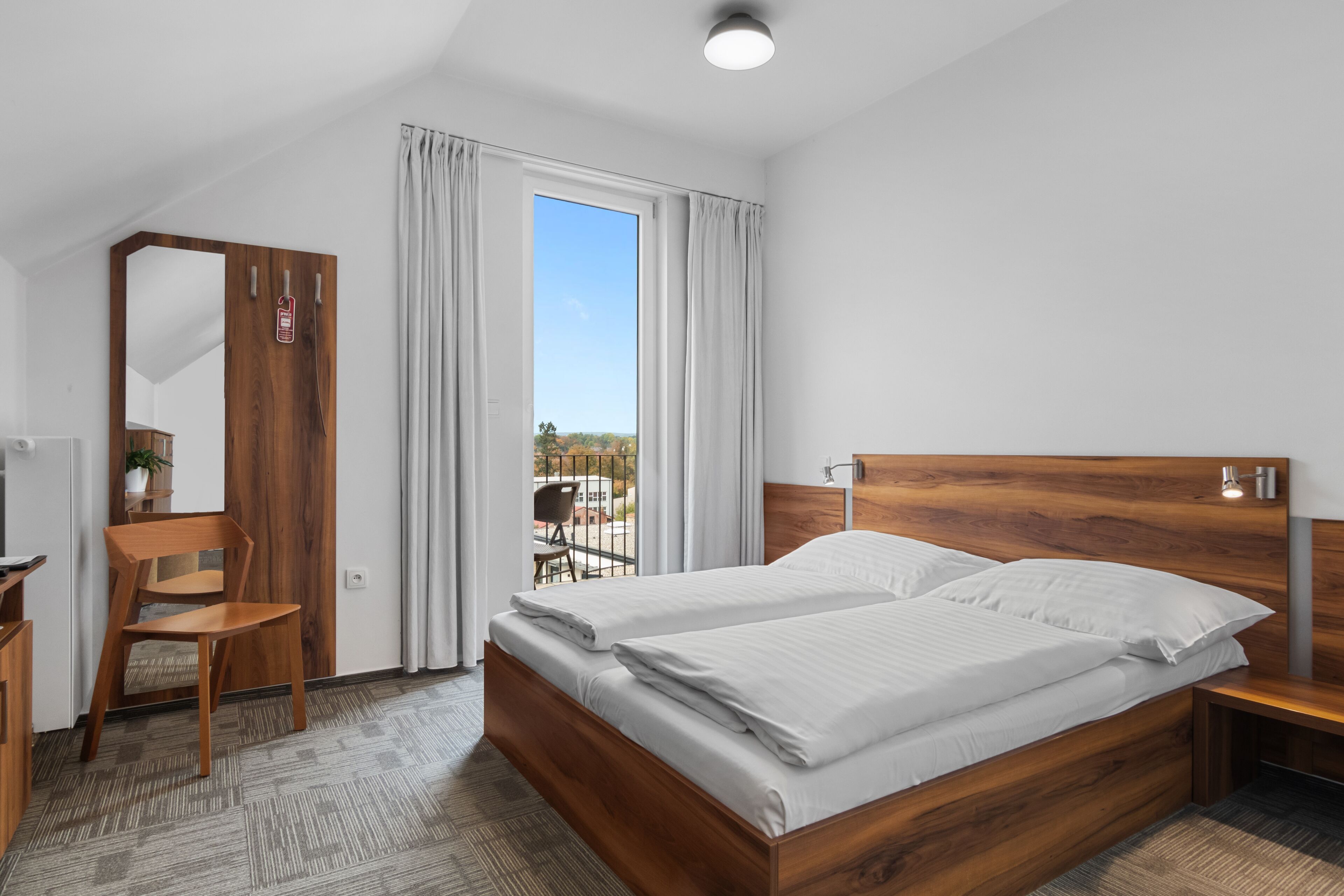 Habitación de hotel moderna con una cama de madera, un escritorio, una silla y vistas al exterior a través de un ventanal grande.