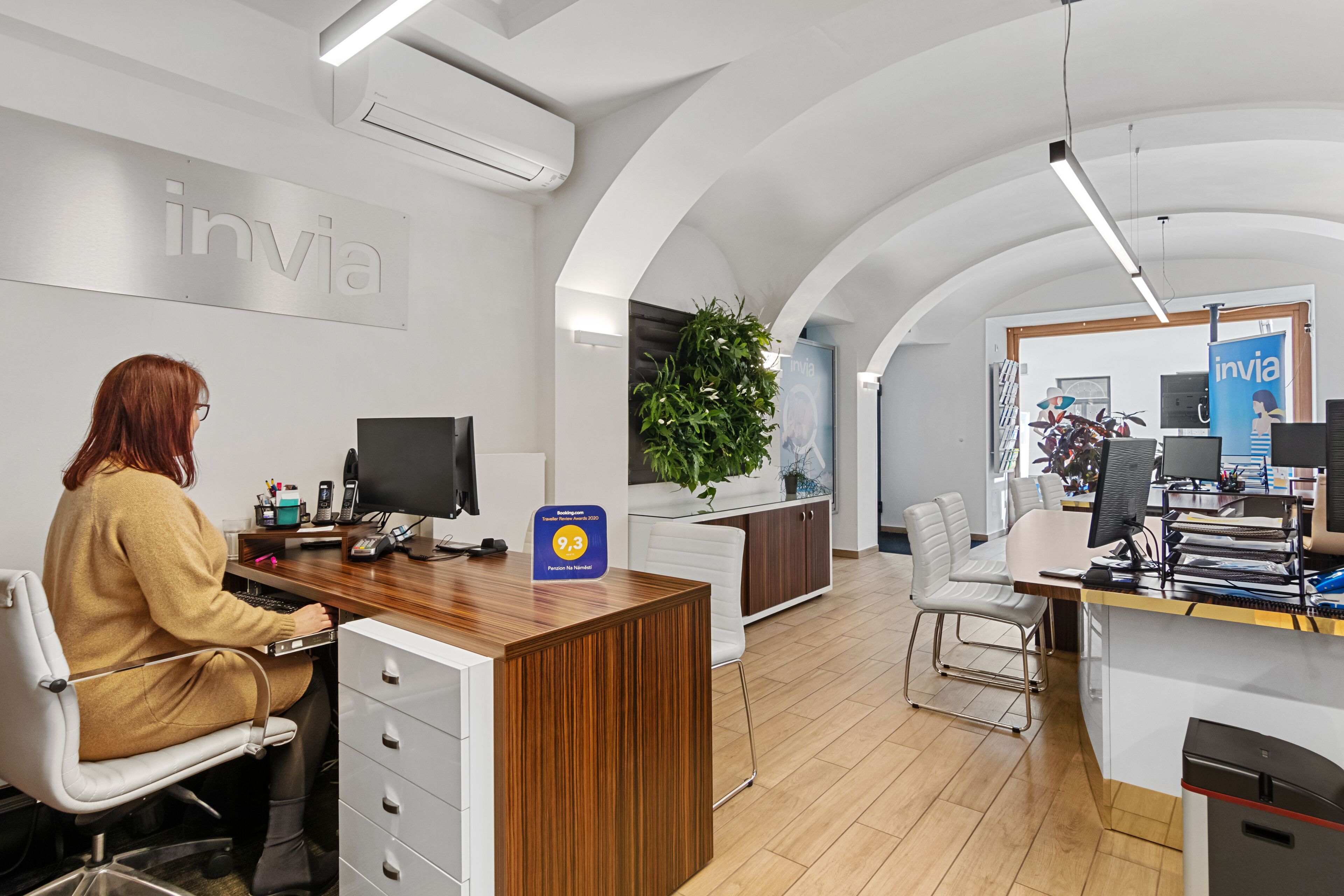 Un bureau moderne avec un comptoir d’accueil, des ordinateurs et une grande plante.