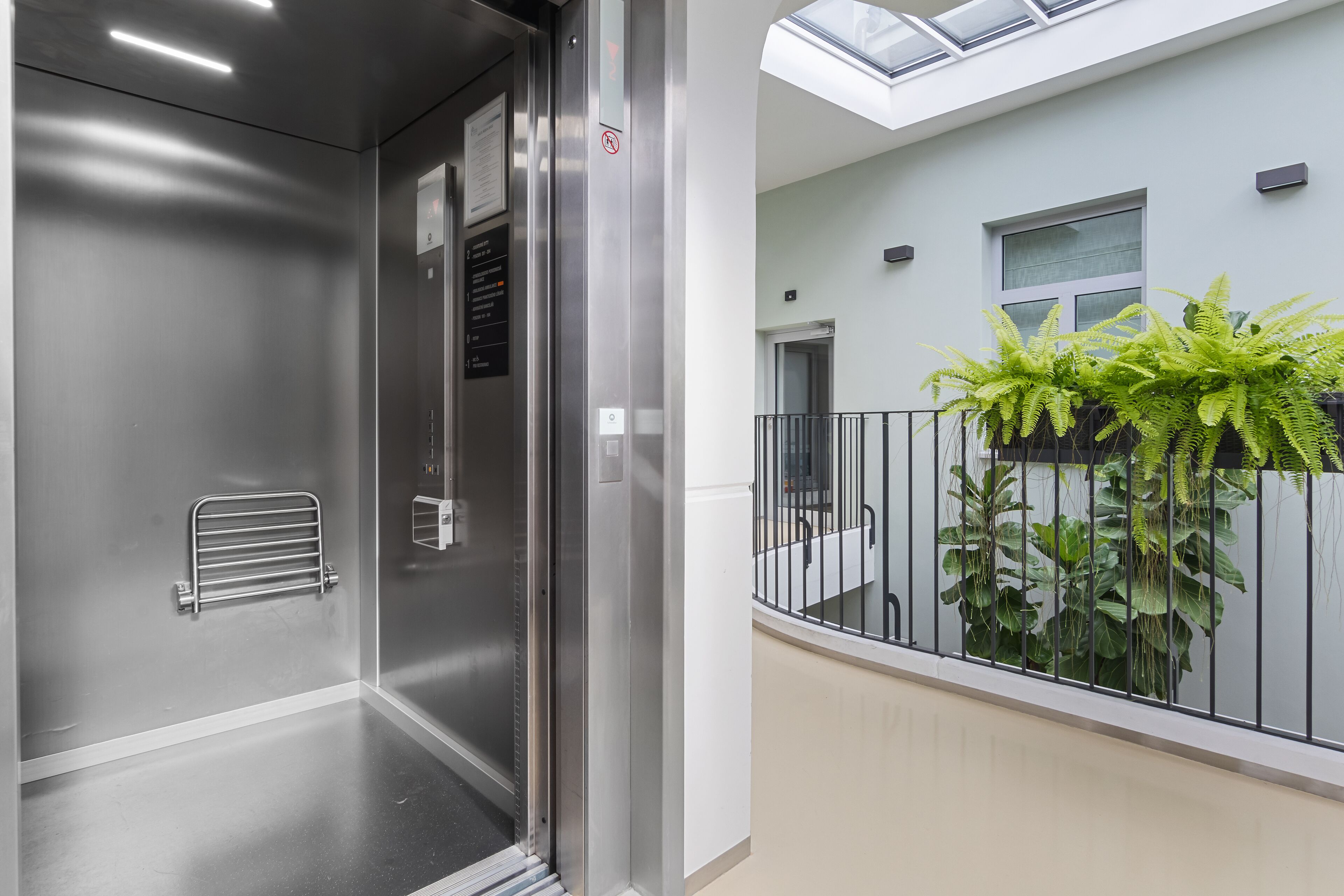 Een moderne lift met een metalen afwerking, een glazen deur en een bedieningspaneel met knoppen.