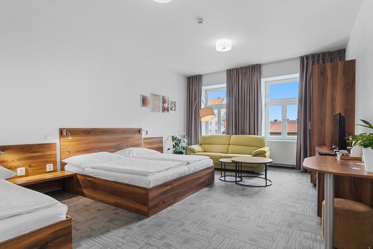 Ein modernes Hotelzimmer mit einem hölzernen Bett, einem gelben Sofa, einem kleinen runden Tisch und einem großen Fenster mit Vorhängen.
