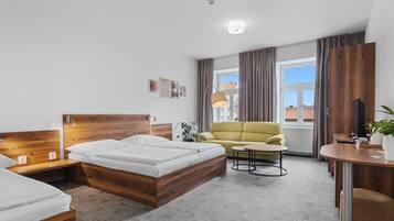 A modern hotel room with a wooden bed, a yellow sofa, a small round table, and a large window with curtains.