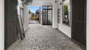 Un étroit sentier pavé de pierres menant à un bâtiment doté d’une entrée moderne, d’un escalier et d’une porte avec un panneau de verre.