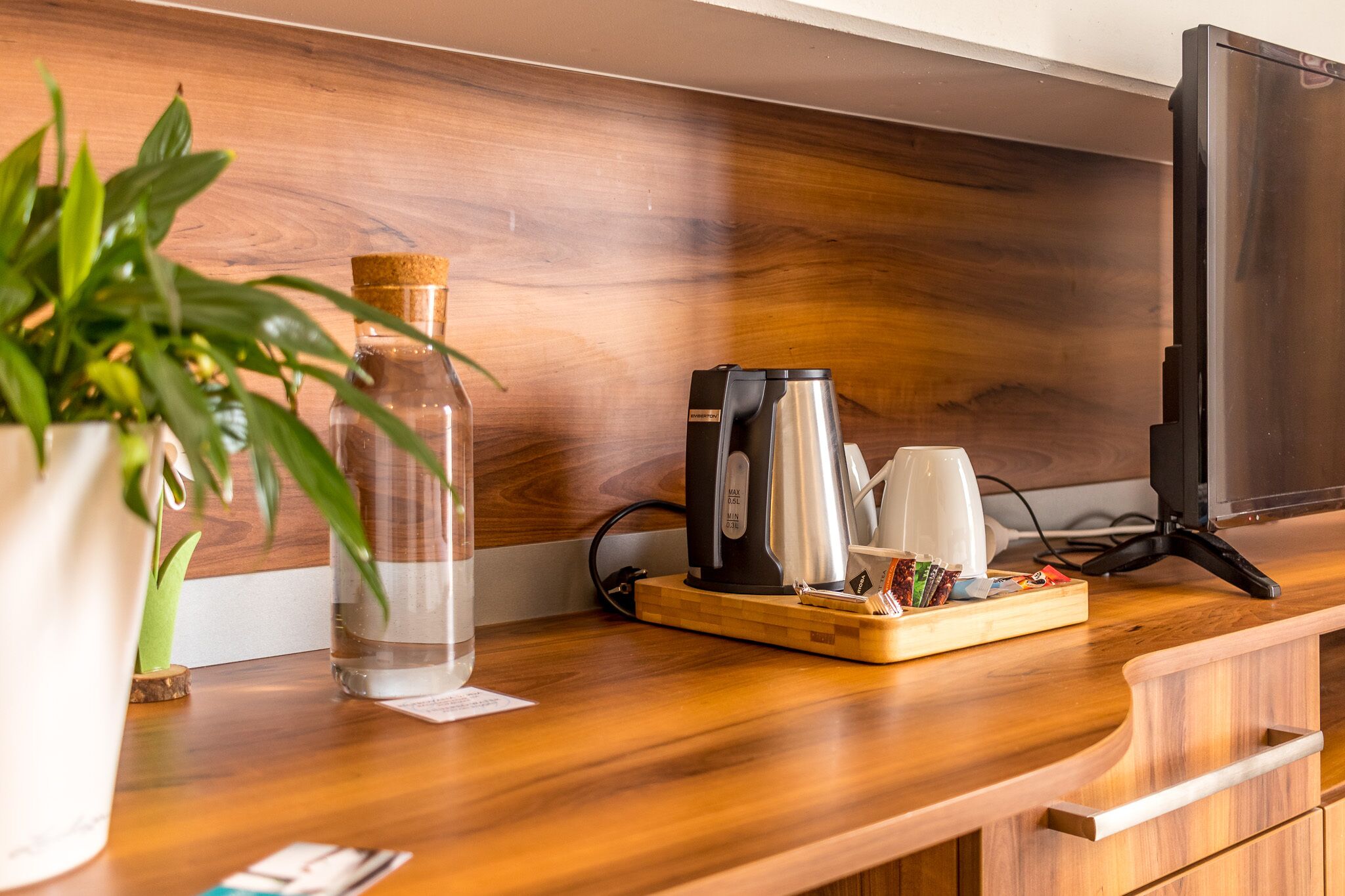 A wooden counter with a coffee maker, a glass bottle, and a tray with coffee cups and utensils.
