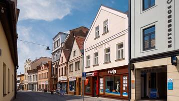 A cobblestone street lined with historic buildings, including a restaurant named 'Penzion' and a shop called 'Invia'.