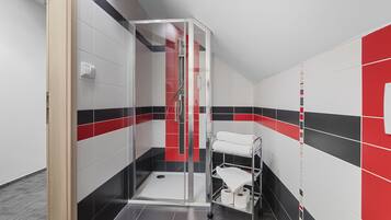 Un baño moderno con cabina de ducha de vidrio, toallero blanco y pared con mosaicos rojos y negros.