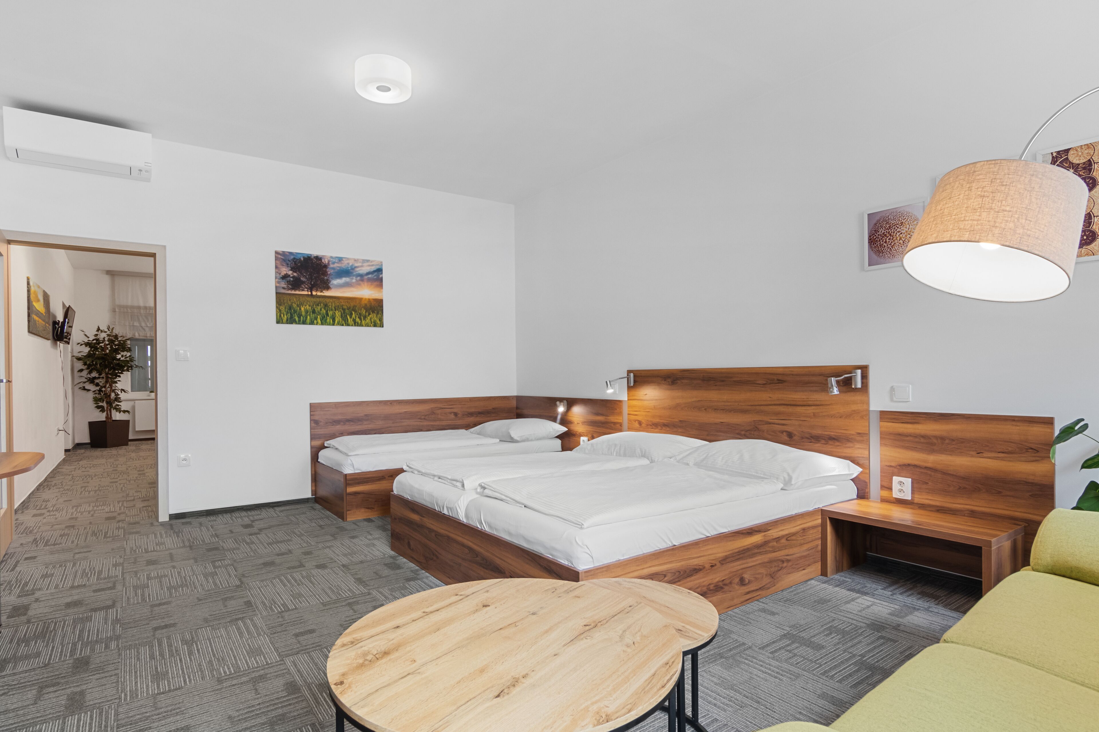 Una habitación de hotel moderna con dos camas de madera, una mesa redonda de madera y un sofá verde.