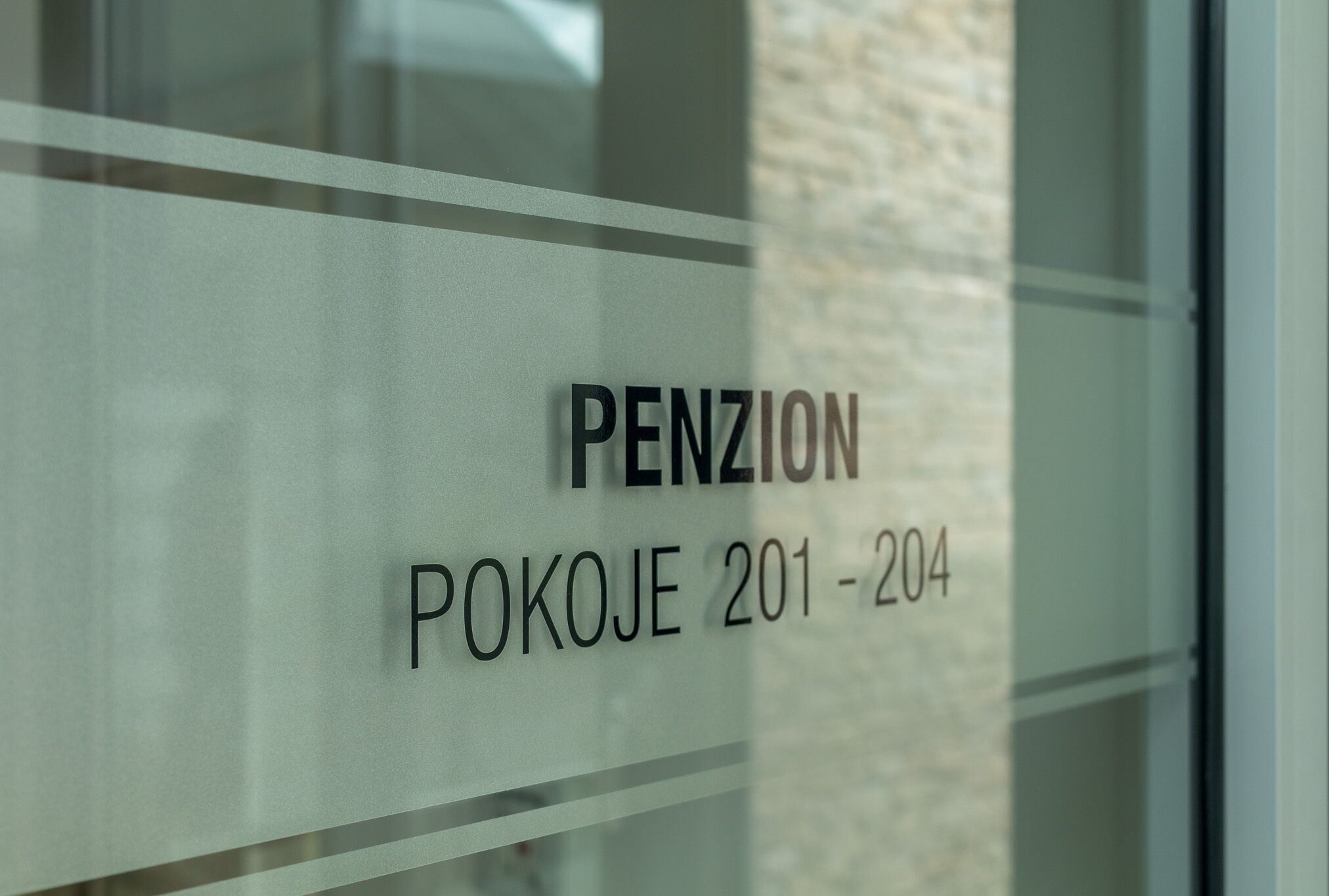 A sign with the text "PENZION POKOJE 201-204" on a glass window.