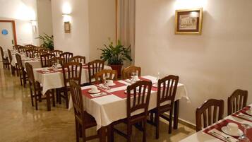 Un comedor con varias mesas, cada una con sillas, manteles blancos y caminos de mesa rojos.