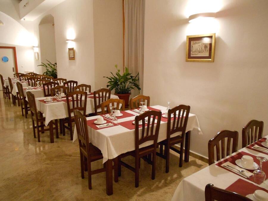 Un comedor con varias mesas, cada una con sillas, manteles blancos y caminos de mesa rojos.