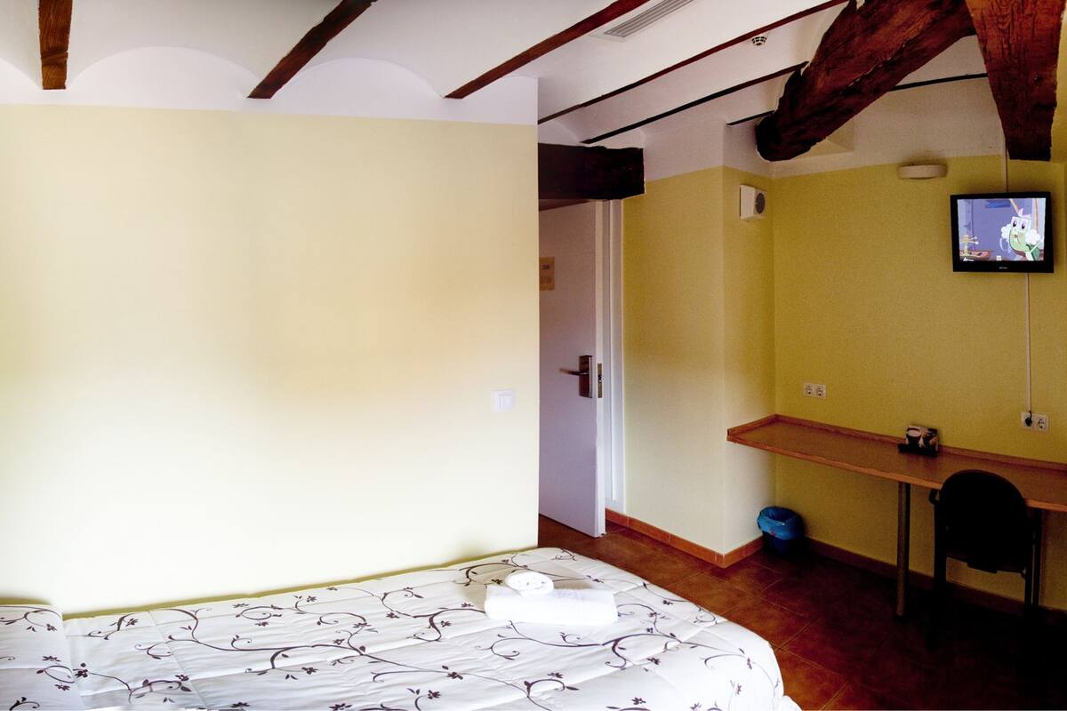 Une chambre à coucher avec un lit, un téléviseur fixé au mur, un petit bureau et une chaise.