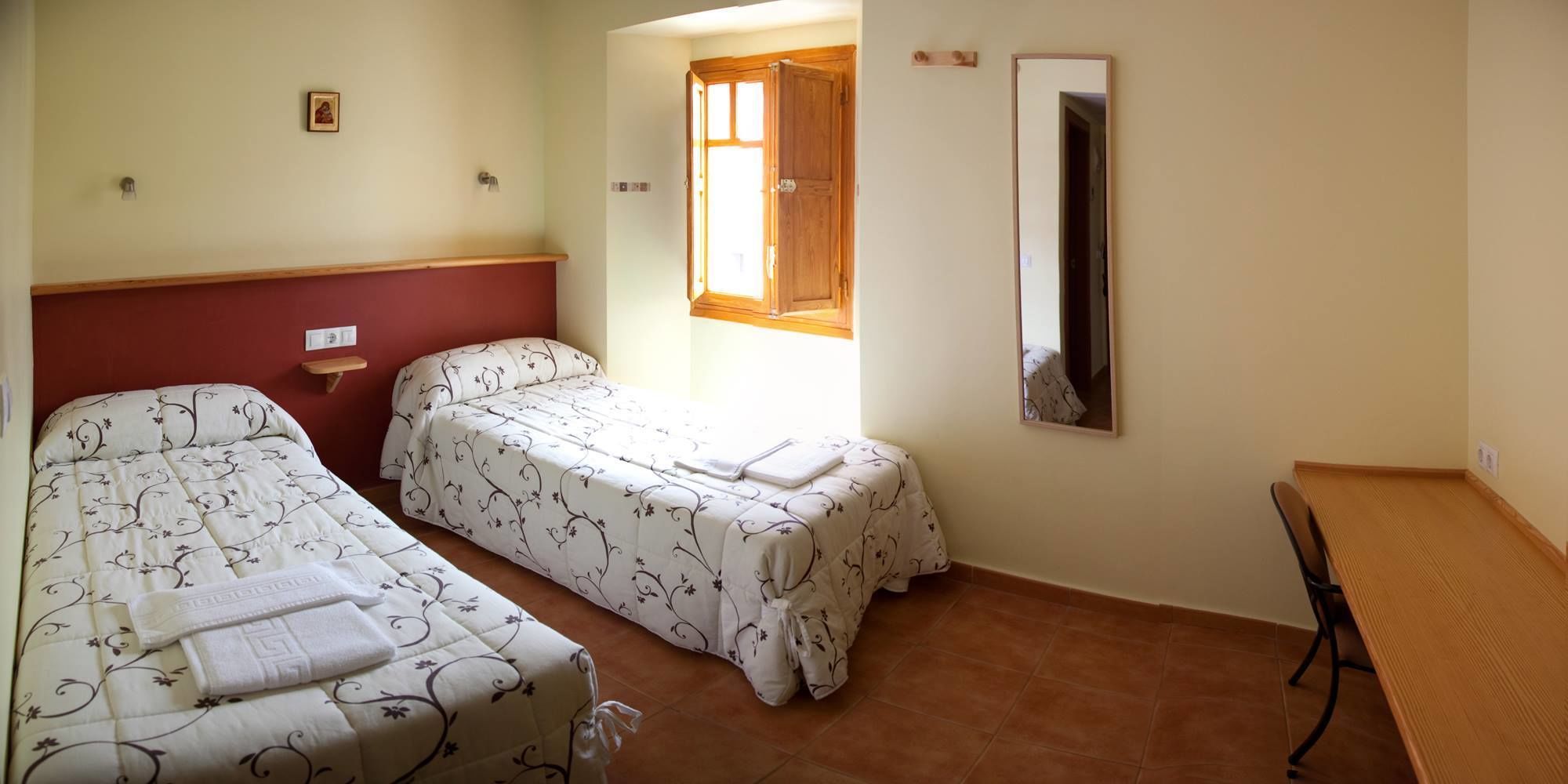Una habitació amb dos llits, un panell de fusta al capçal, una taula petita i un mirall a la paret.