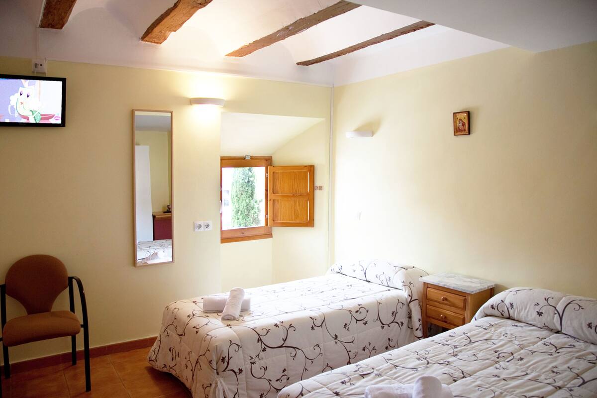 Une chambre d’hôtel avec deux lits, une chaise, une petite table, un miroir et un téléviseur.