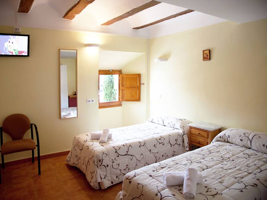 Habitación de hotel con dos camas, una silla, una mesita, un espejo y un televisor.