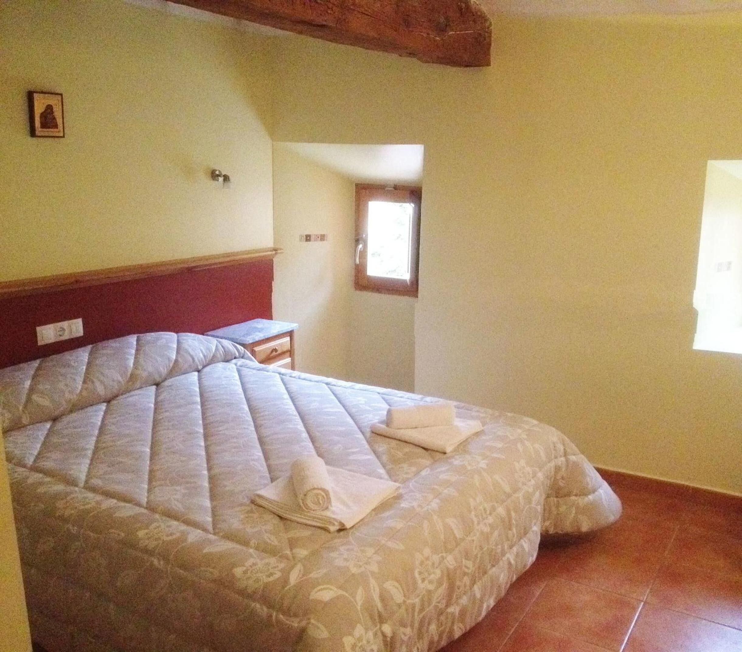 Een slaapkamer met een groot bed, een klein tafeltje en een raam.