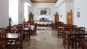 A spacious dining hall with wooden tables and chairs, a large painting on the wall, and a polished floor. - Hospedería Nuestra Señora del Carmen (Caravaca de la Cruz)