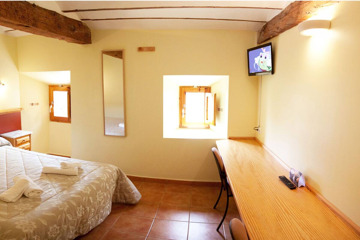 Une chambre à coucher avec un lit, une table de chevet, un miroir, une télévision et une fenêtre.