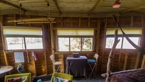 A rustic cabin interior with wooden walls, a dining table, two chairs, a small table, and a hanging light fixture. - Bamff Ecotourism (Blairgowrie)