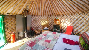 A yurt interior with a bed, a small heater, a lantern, and a firewood storage area. - Bamff Ecotourism (Blairgowrie)